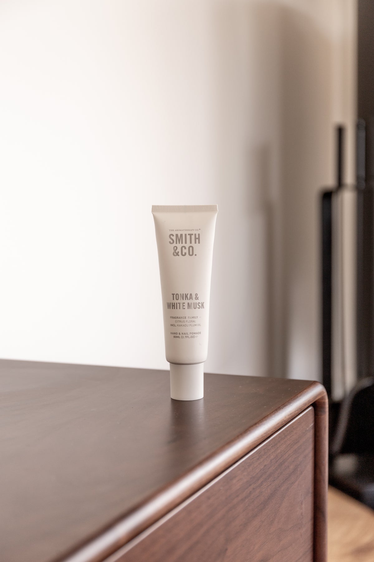 Hand cream tube on the corner of a dark timber cabinet in a pale, quiet room