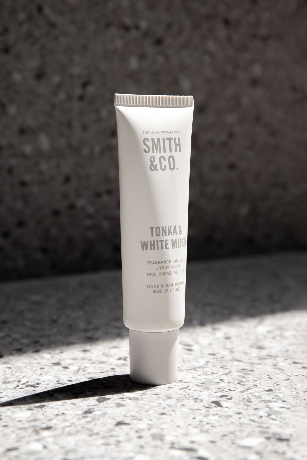 Hand cream tube in bright sunlight on grey terrazzo with a dark speckled wall behind
