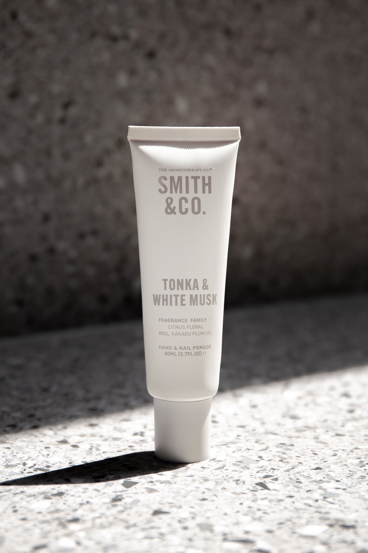 Tonka and White Musk hand cream on terrazzo, casting a sharp shadow in direct sun