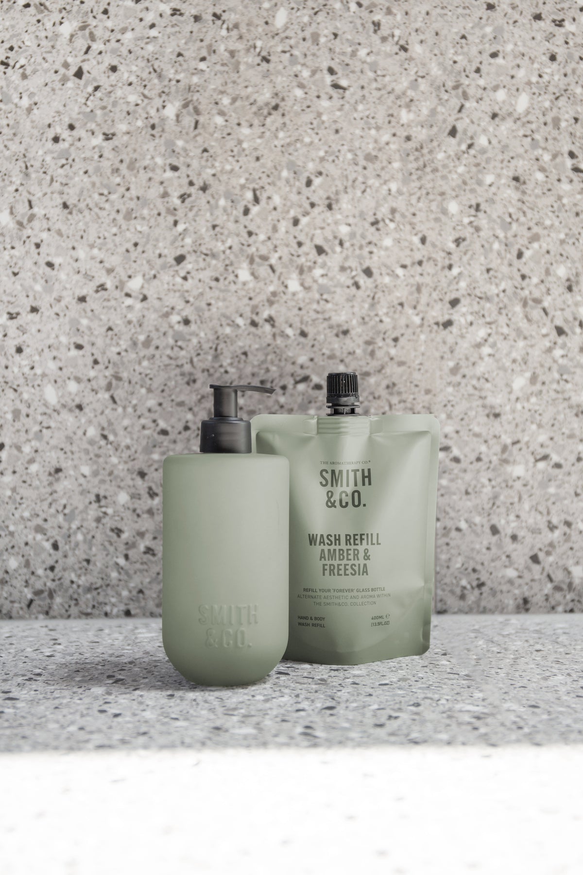 Two sage green Smith & Co. bottles on a terrazzo surface, close up