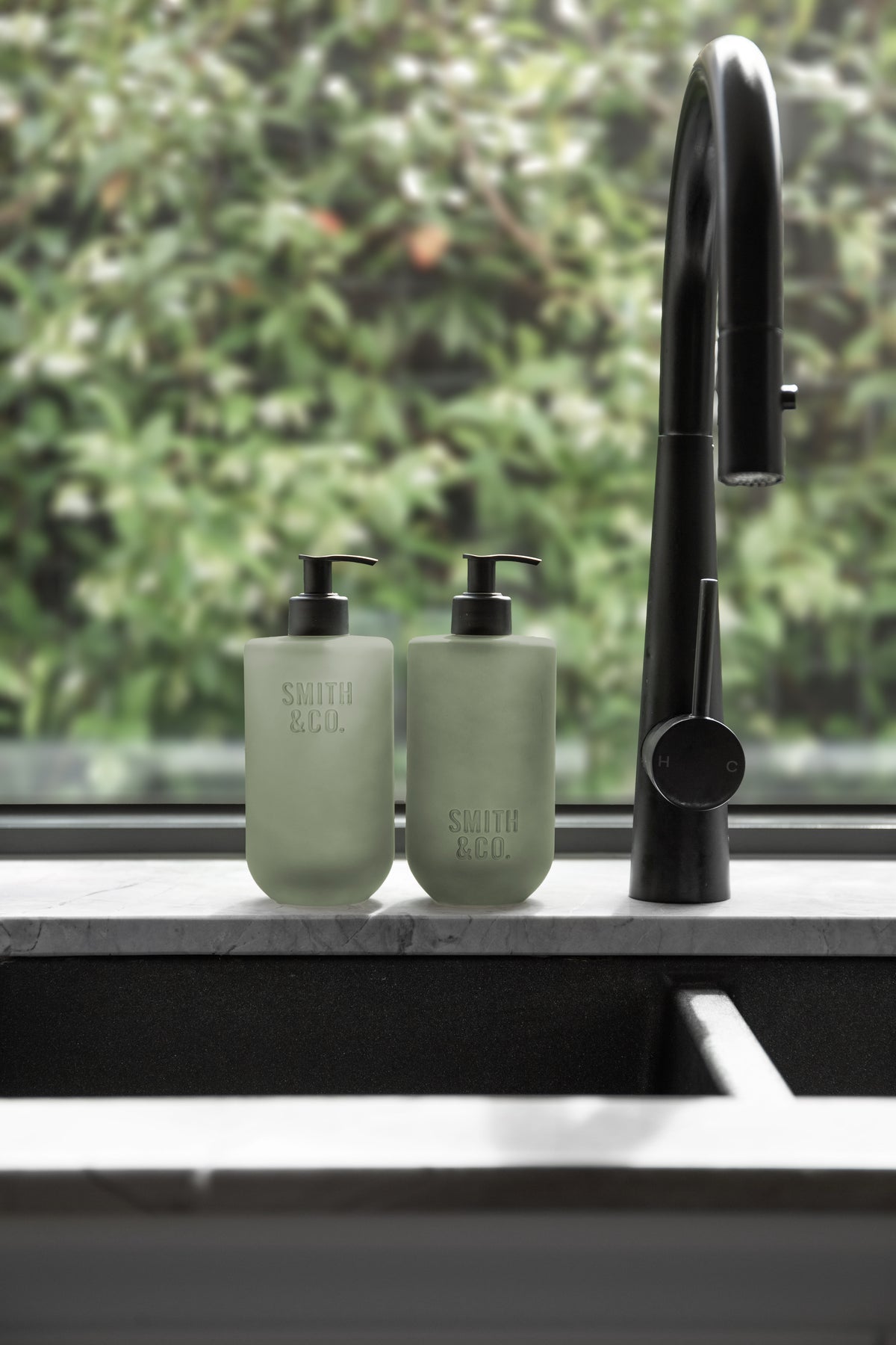 Pair of sage green pump bottles beside a black tap and sink, close view