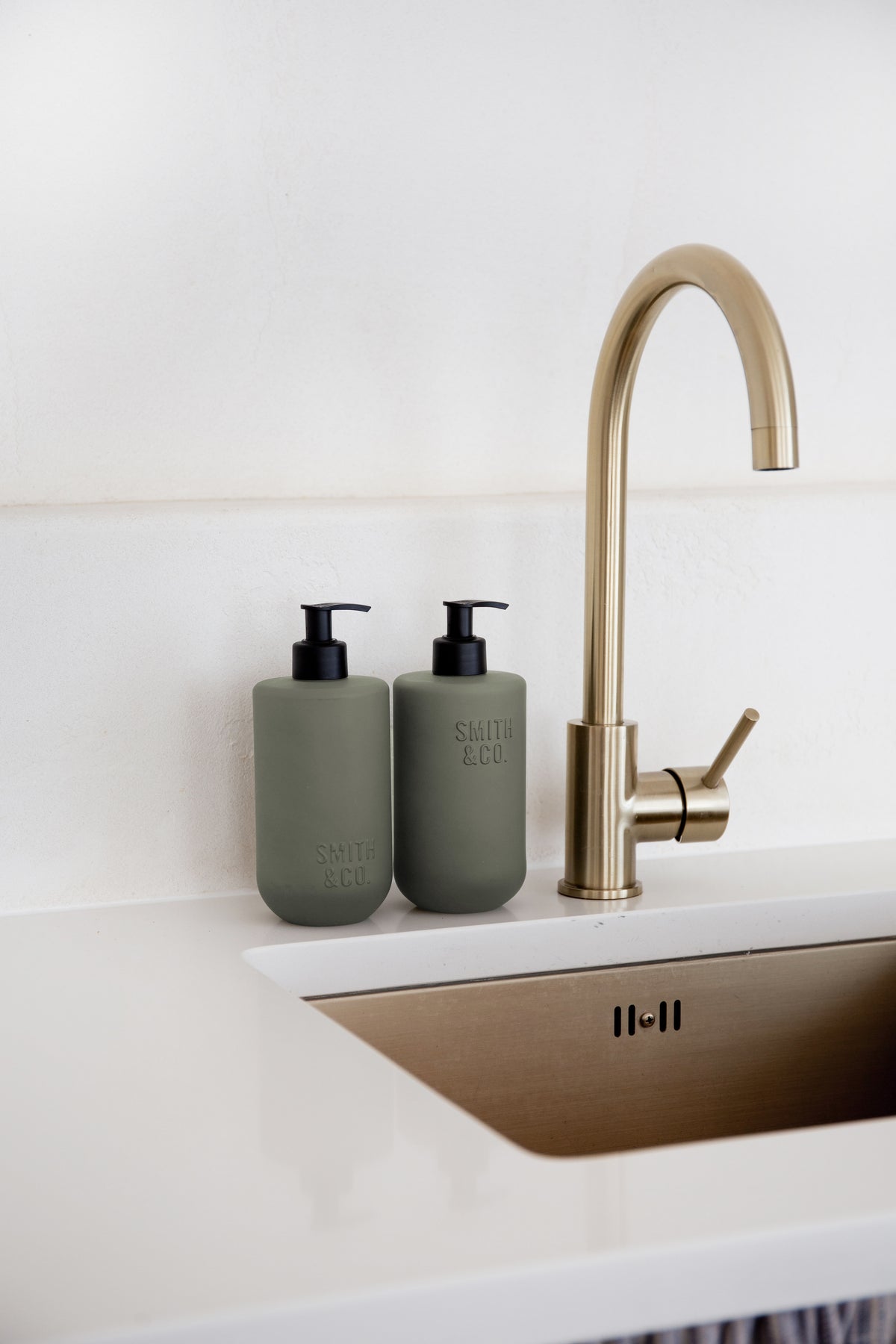 Sage green bottles beside a brass tap on a pale benchtop