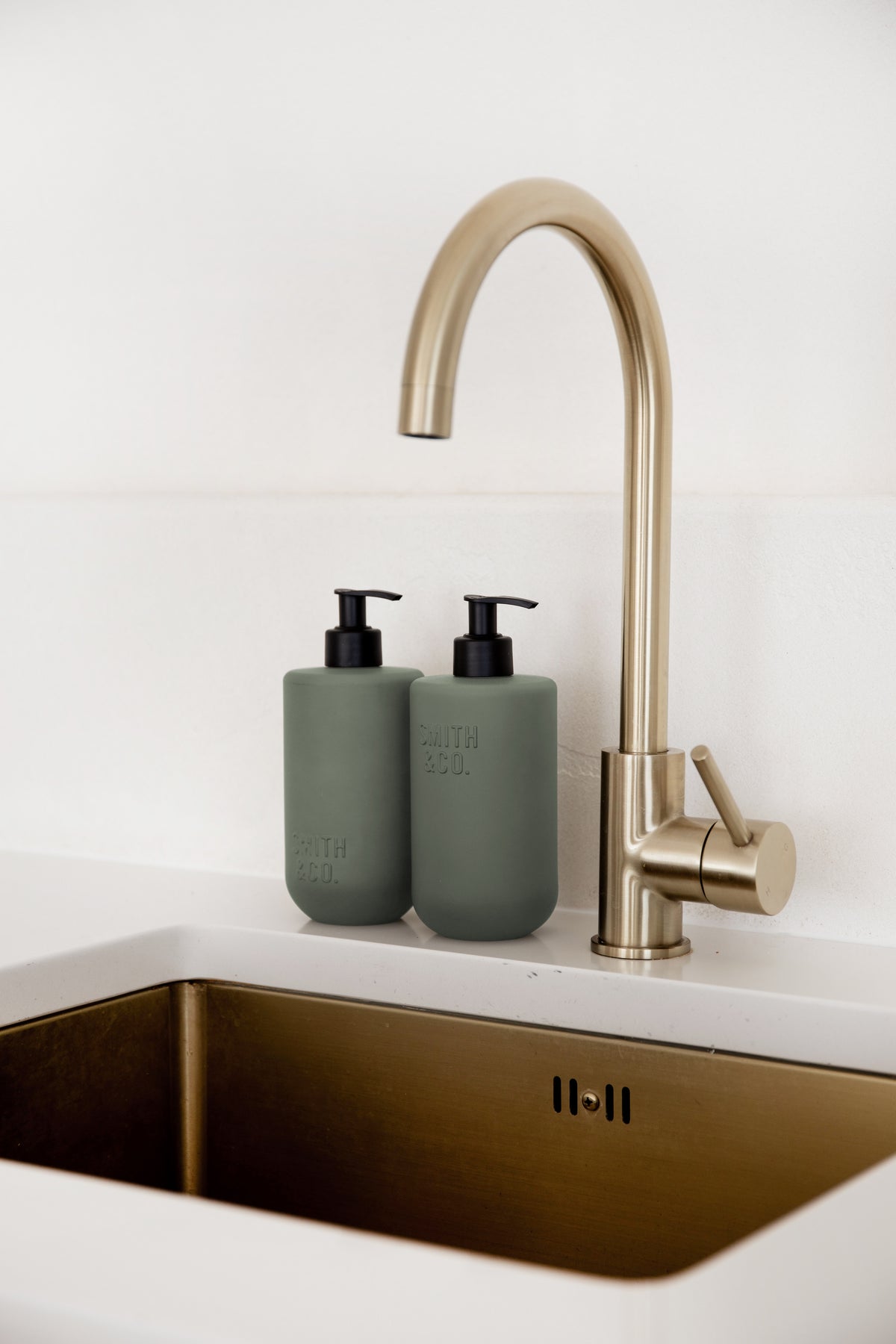 Sage green pump bottles by a brass gooseneck tap over a brass sink