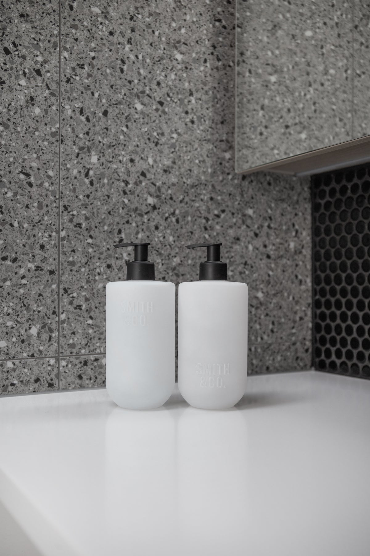 Two frosted Smith and Co bottles on a white bench against grey terrazzo tiles