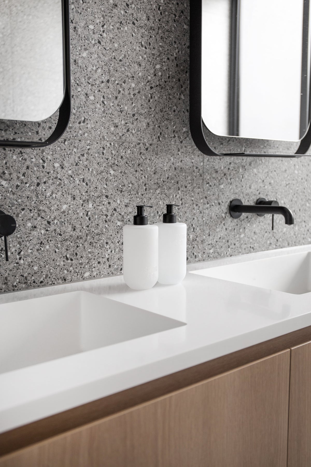 Smith & Co. bottles on a white vanity with timber drawers, terrazzo wall and black mirrors