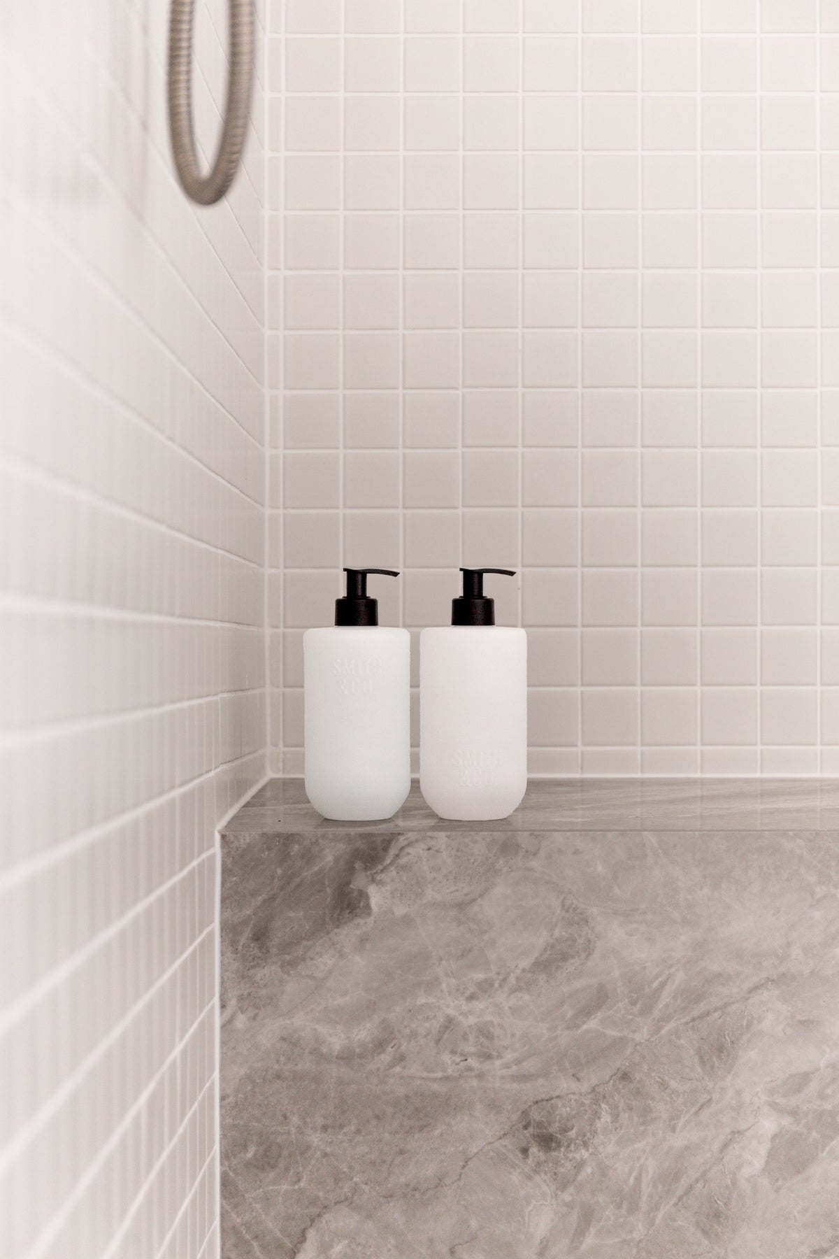 Two Smith & Co. bottles on a stone shower seat against white tiles