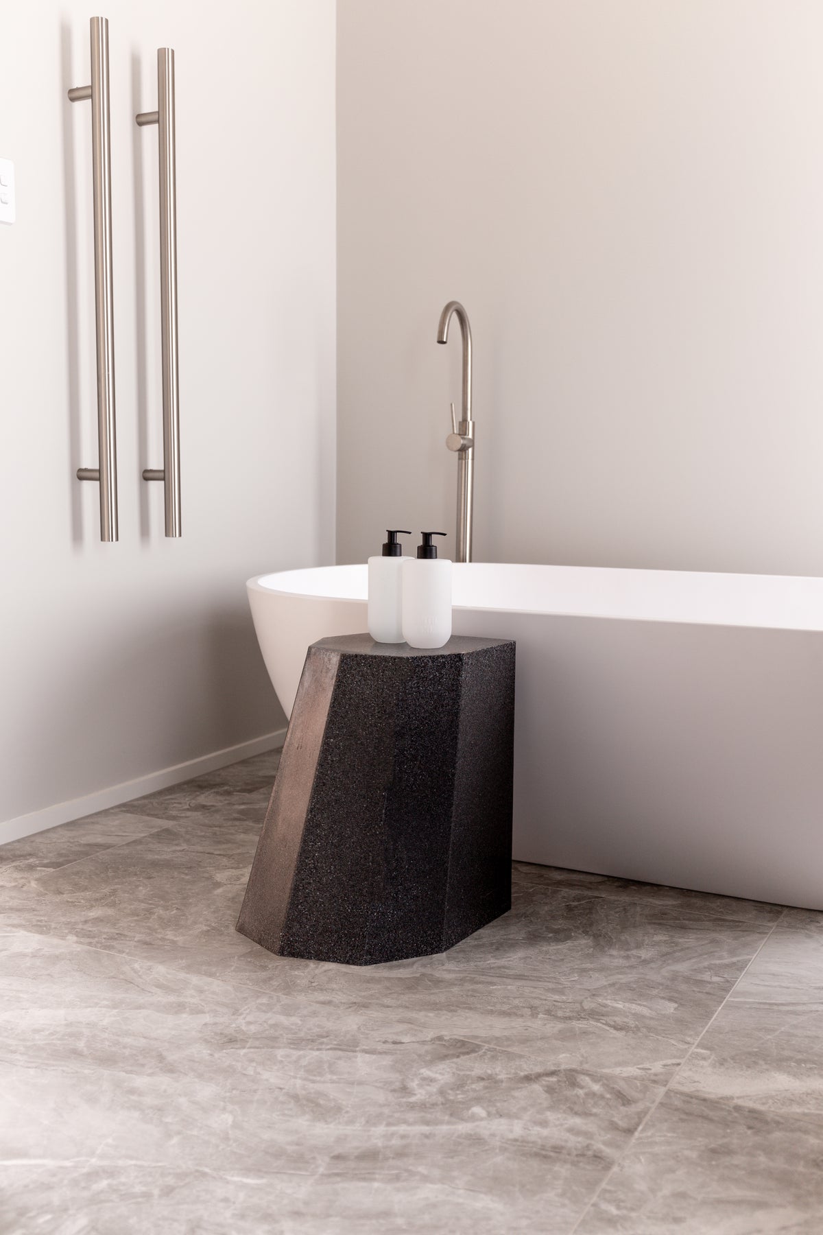 Smith & Co. bottles on a dark sculptural stool beside a freestanding bath and brass towel rail