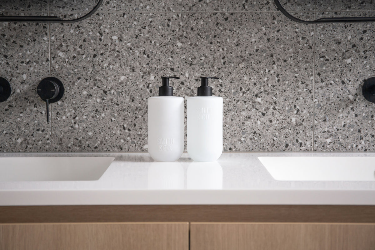 Two Smith & Co. bottles centred between twin basins on a terrazzo-backed vanity