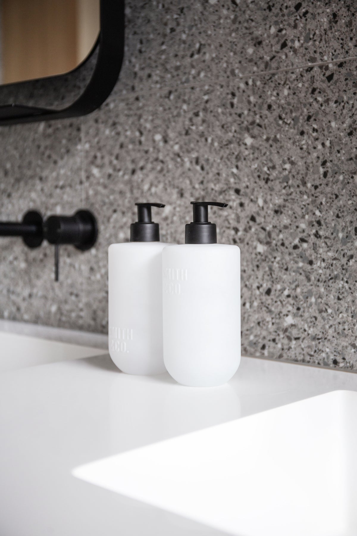 Smith & Co. pump bottles on a white vanity against grey terrazzo with a black wall mixer
