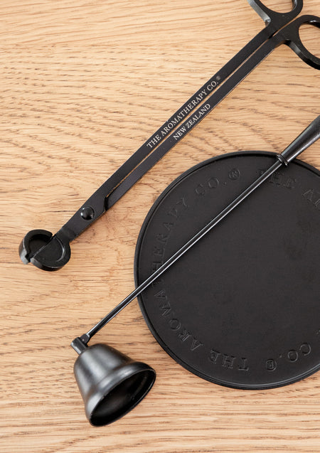 Black candle snuffer and wick trimmer laid across an embossed black plate, from above
