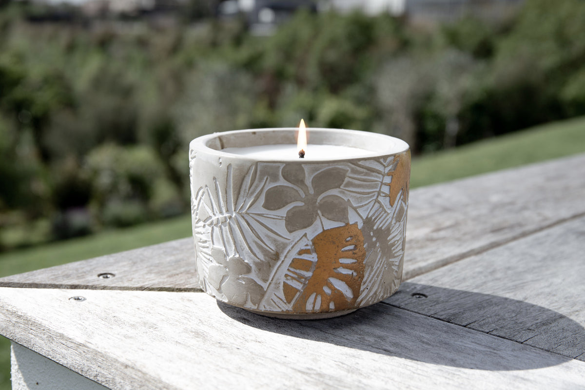 Lit candle on a timber deck rail with green bush in the background