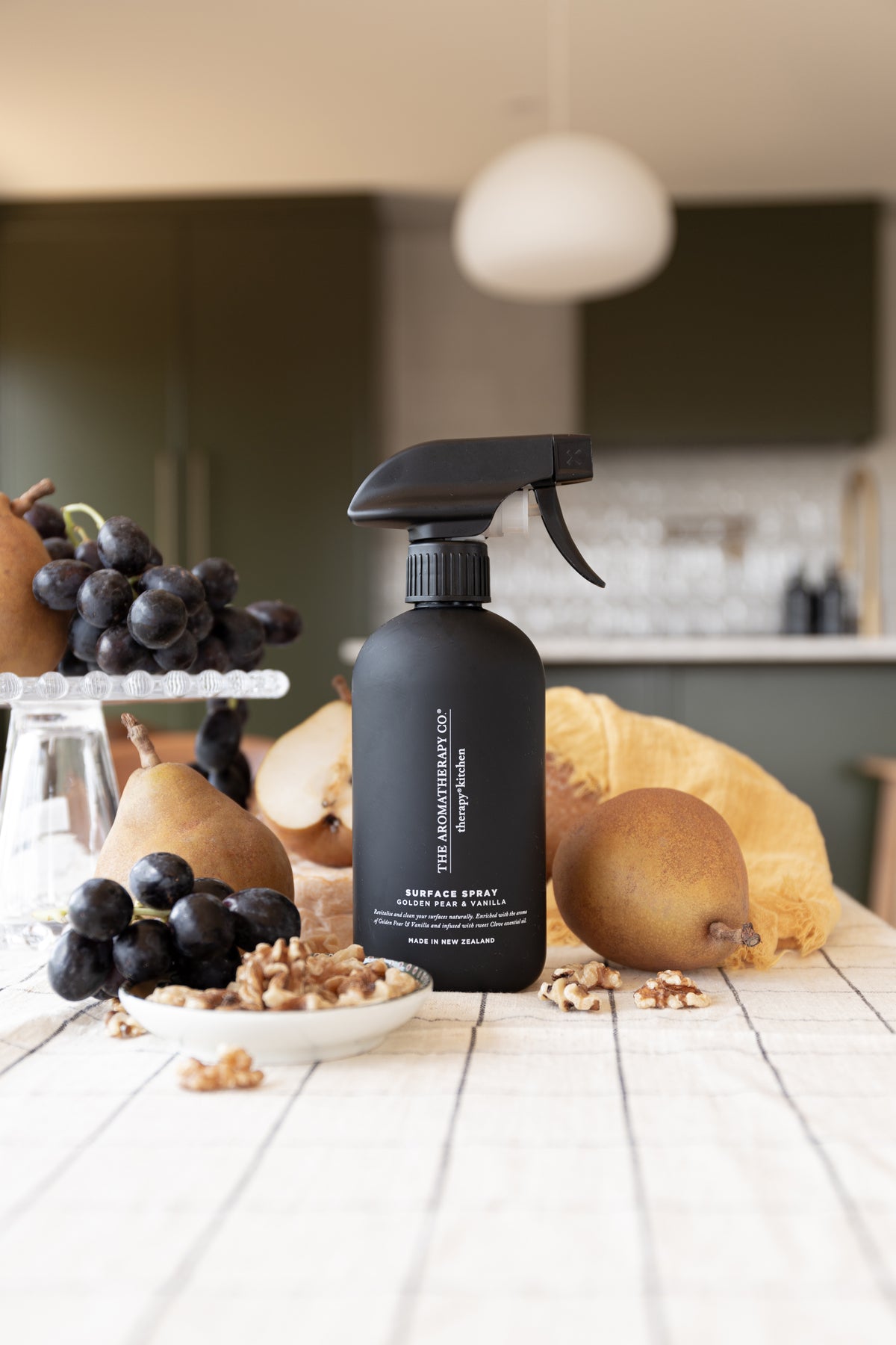 Black surface spray among pears, grapes and walnuts on a white table beneath a pendant light