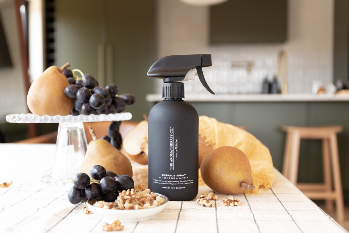 Black surface spray on a white table with pears and grapes on a cake stand in an olive kitchen