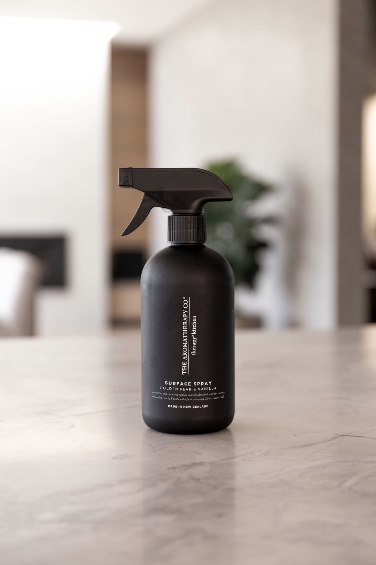 Black surface spray bottle on a marble benchtop with a blurred living room behind