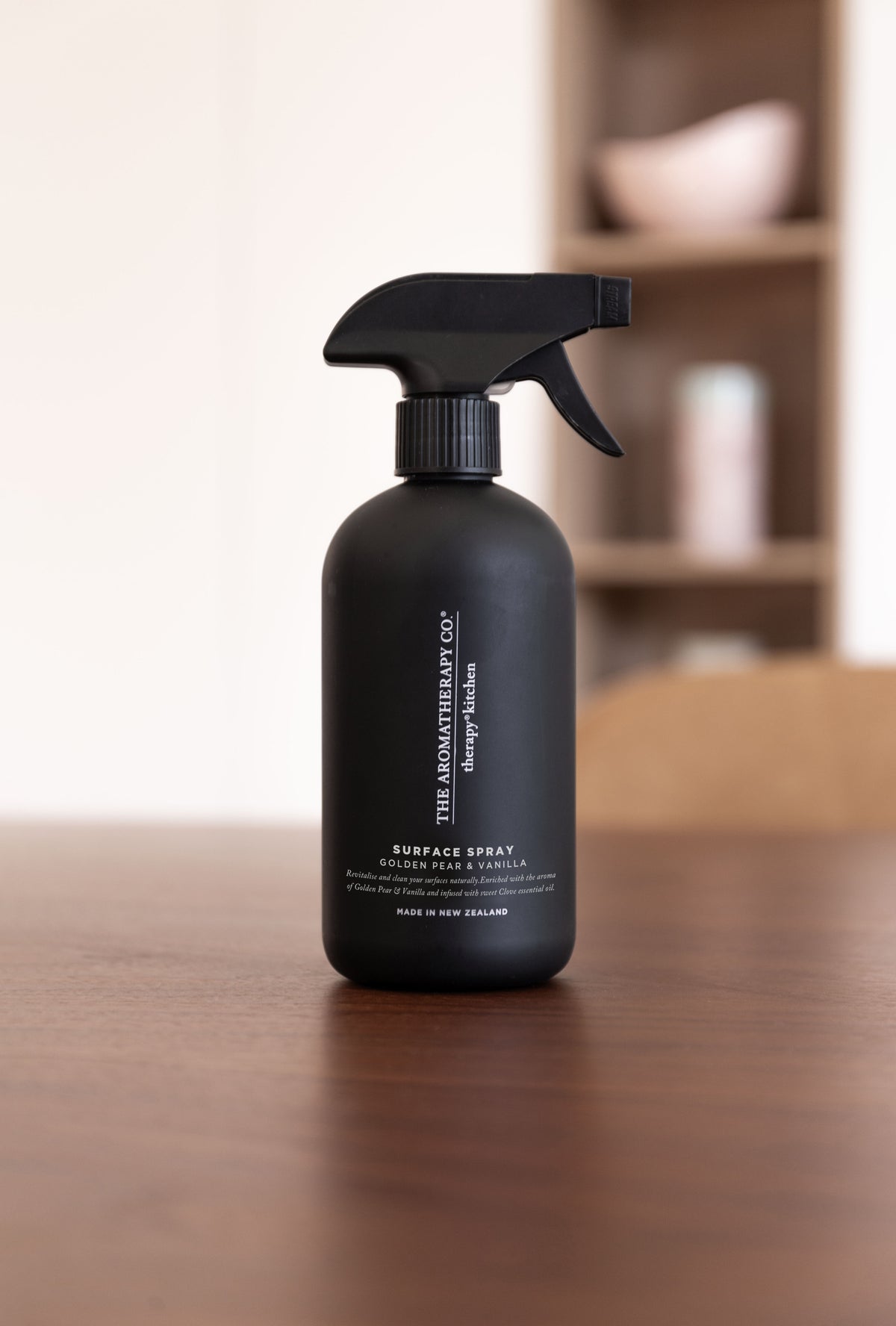 Black surface spray bottle on a dark timber table in front of pale shelving
