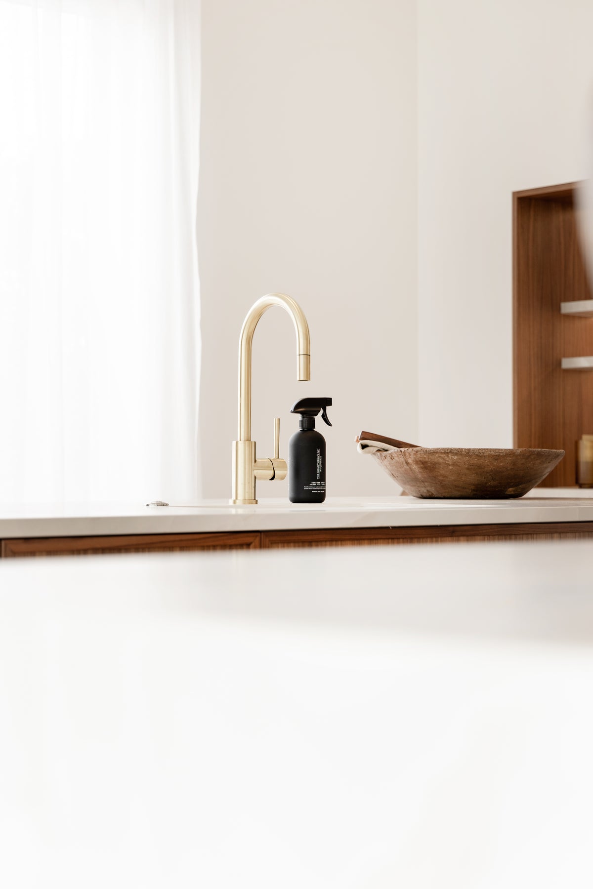 Black surface spray at a white kitchen sink with a brass tap and a carved wooden bowl