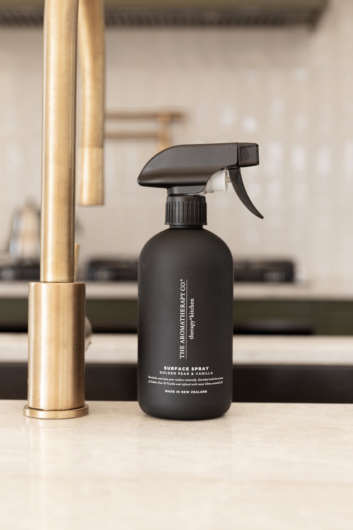 Black surface spray beside a brass tap on a pale benchtop with a tiled splashback