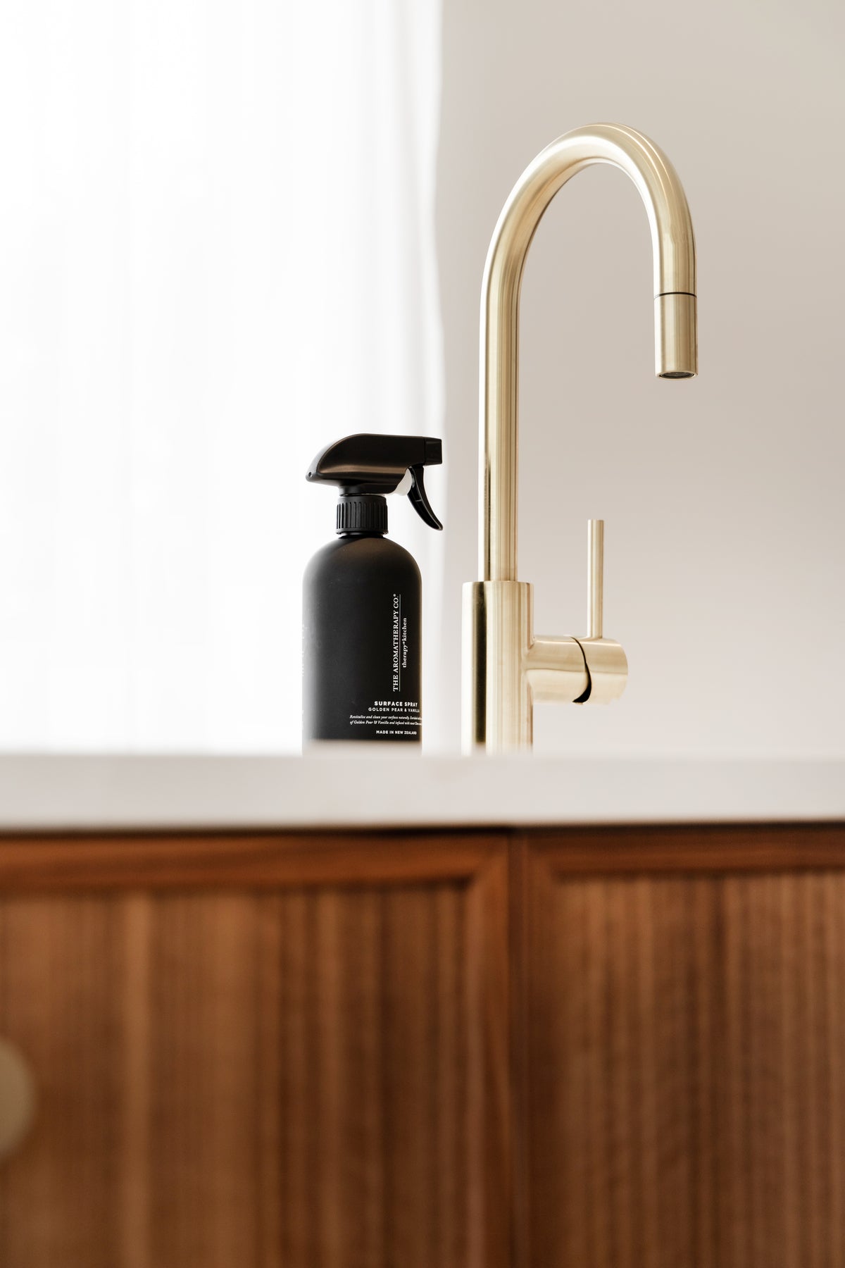 Black surface spray and a brass tap on a white benchtop above warm timber cabinetry