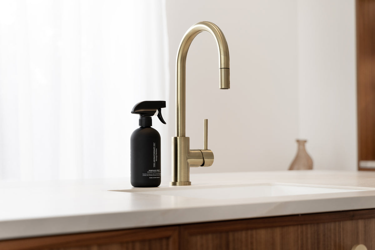 Black surface spray by a brass tap on a white benchtop above fluted timber cabinetry