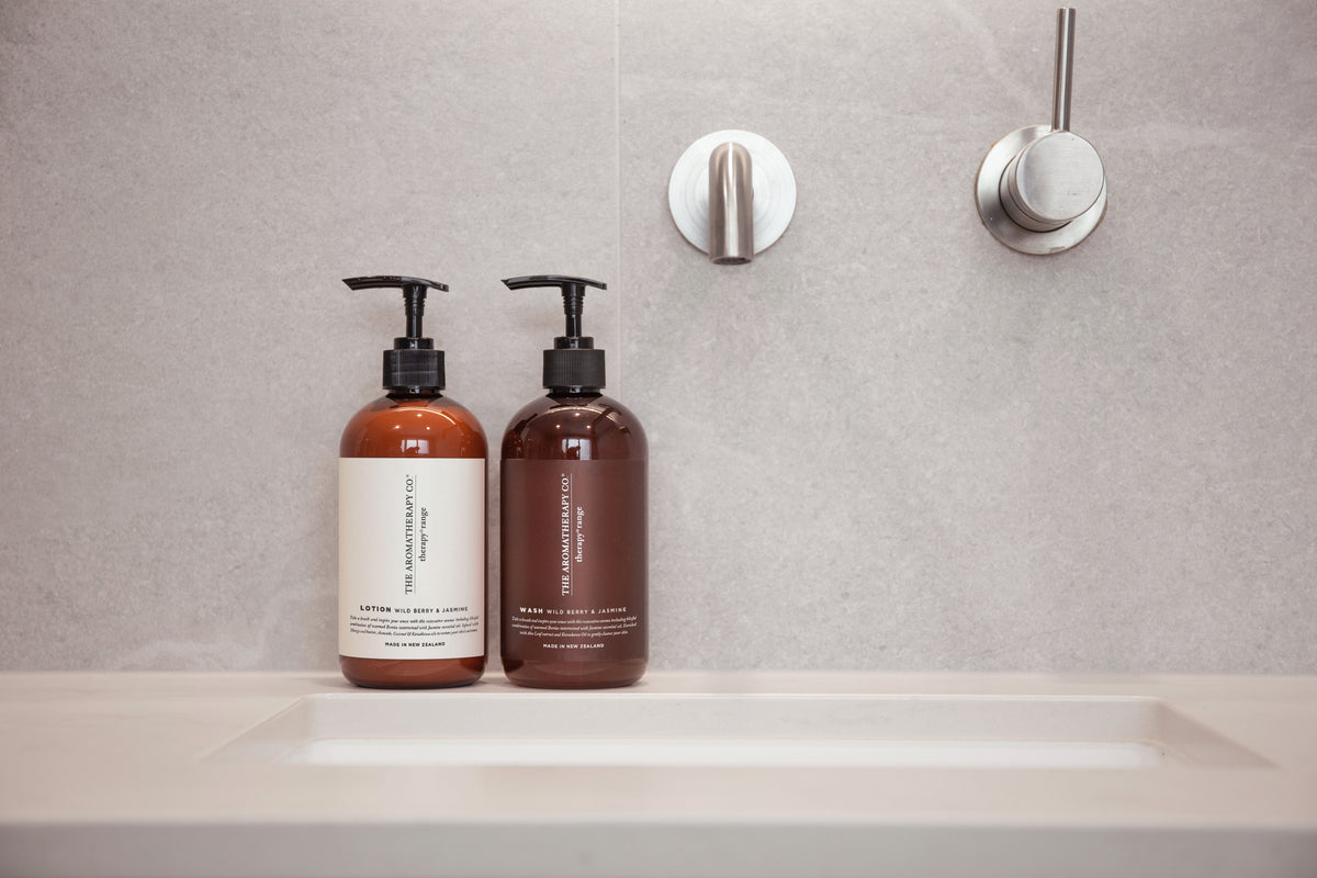 Two amber Therapy pump bottles on the edge of a stone bath surround, wall mounted tapware behind