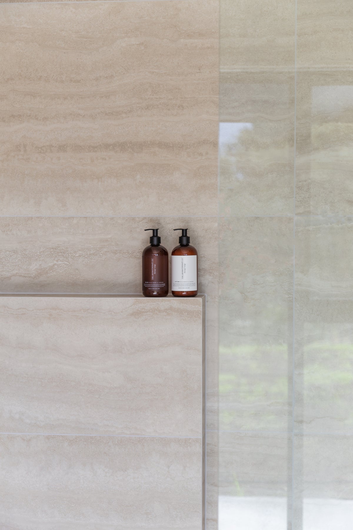 Stone tiled shower with a recessed ledge holding two small amber pump bottles