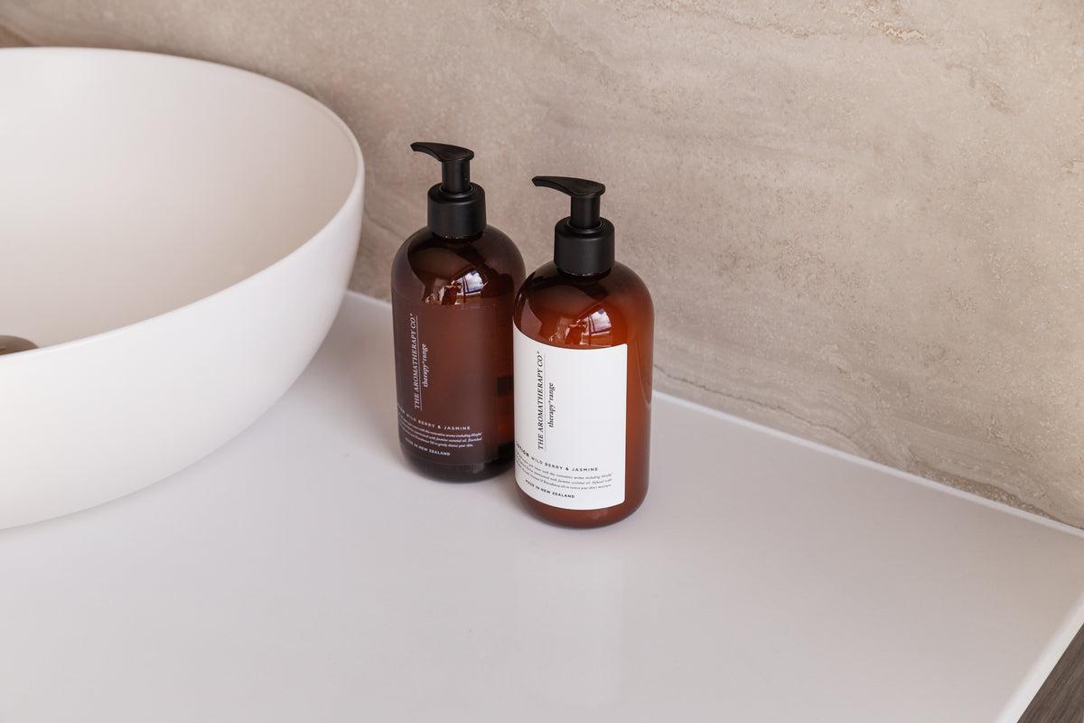 Amber pump bottles beside a round white basin on a pale stone benchtop