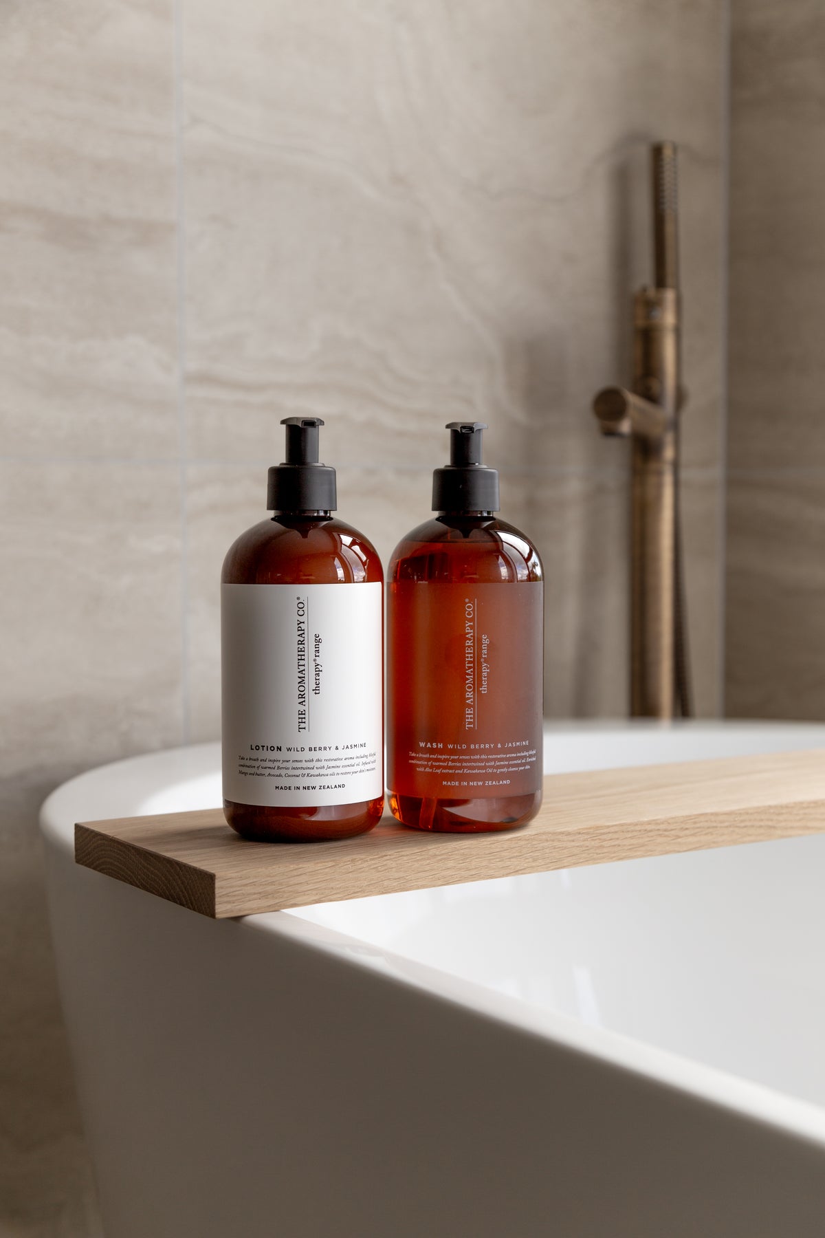 Two amber Therapy pump bottles on a timber board laid across a freestanding bath