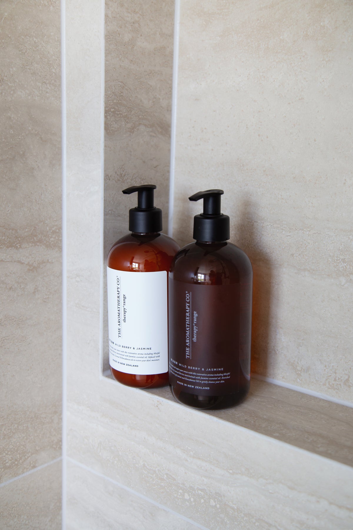 A pair of amber pump bottles standing in a tall stone tiled recess