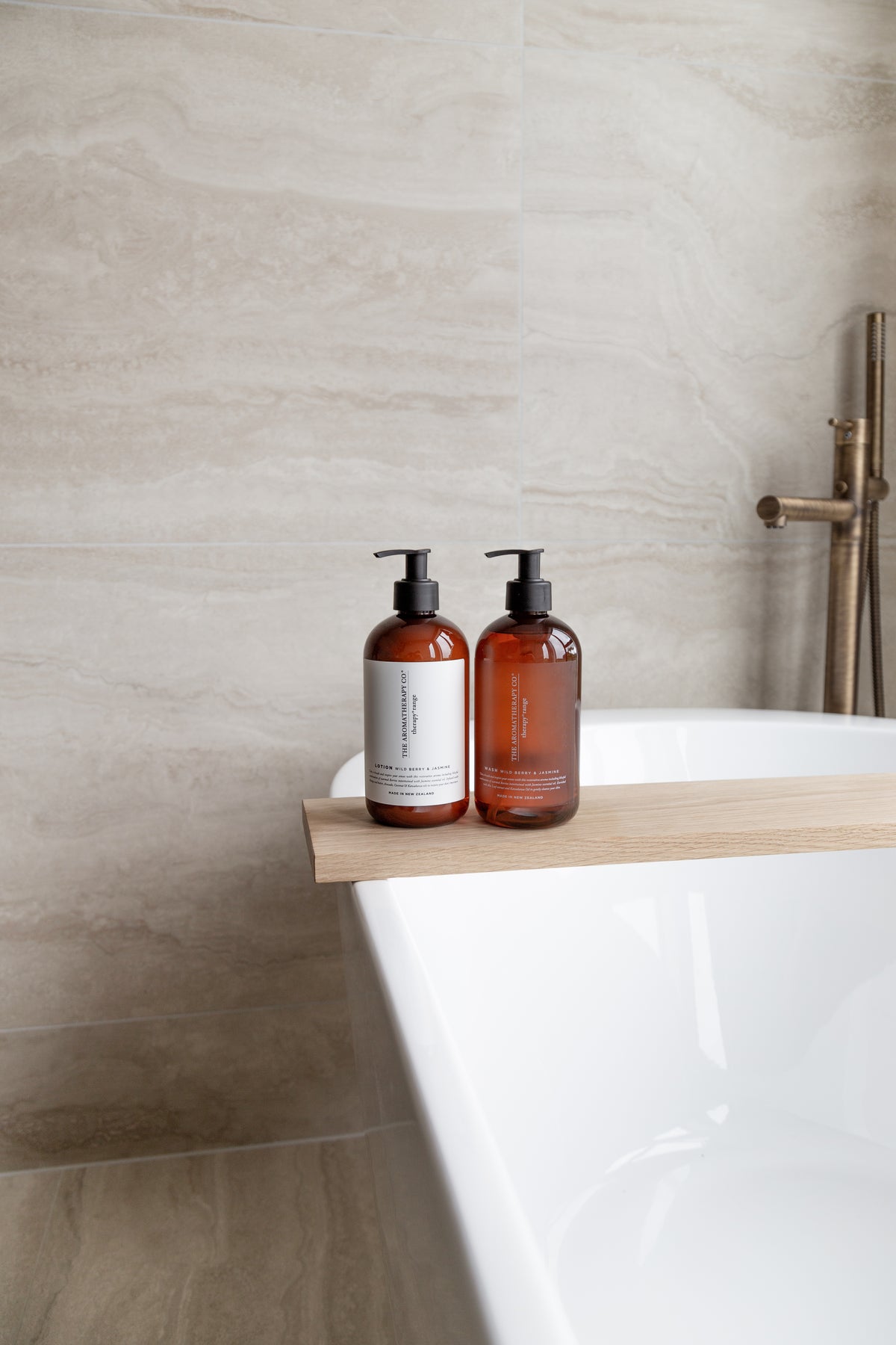 Freestanding bath with a timber board holding two amber pump bottles, floor mounted tap behind