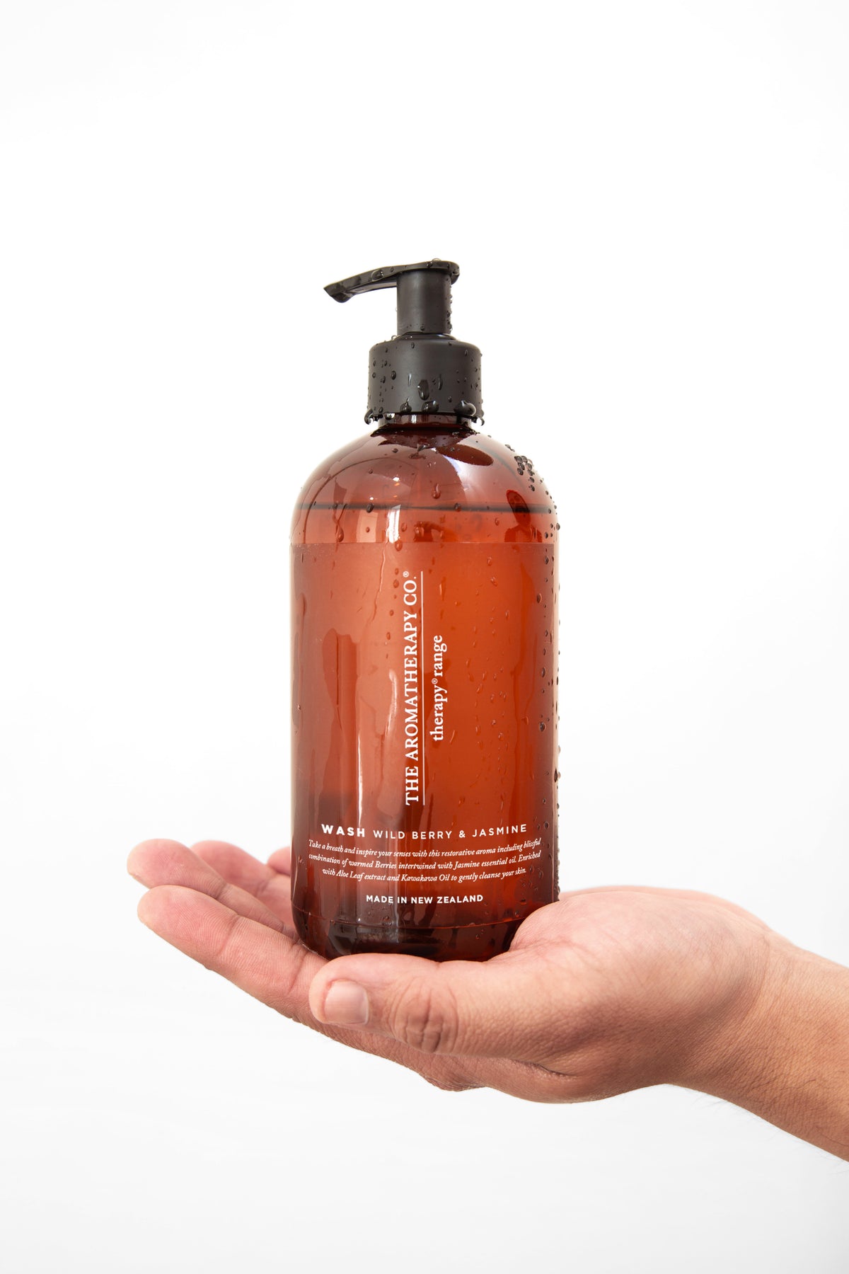 An open hand holding a large amber Therapy pump bottle against a plain white background