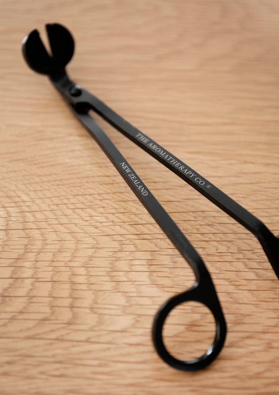 Black wick trimmer lying alone on light oak, the angled blade and one finger loop in view
