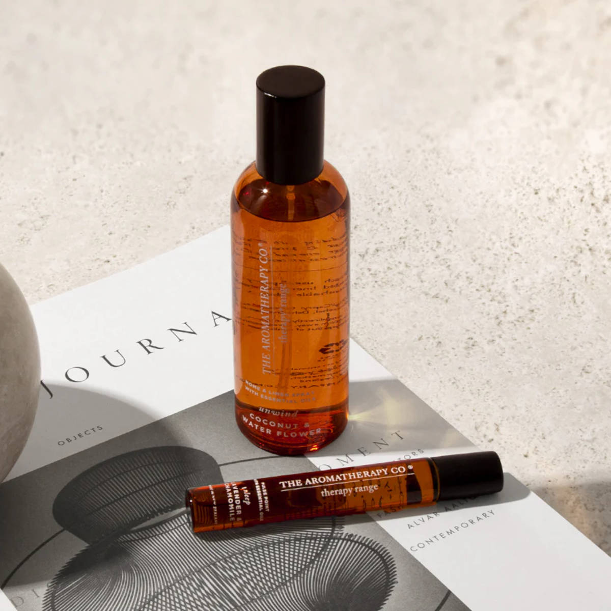 Amber room spray and a matching rollerball on an open journal beside a stone sphere
