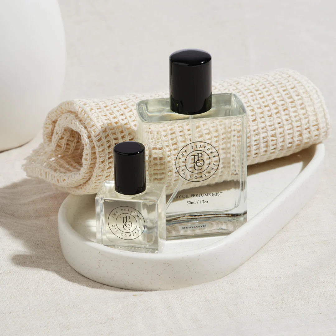 Perfume oil bottle on a ribbed stone dish beside a rolled waffle towel