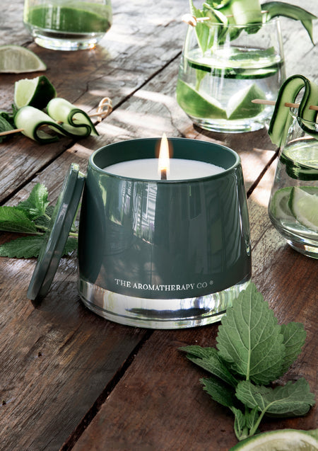 Lit green candle on a rustic timber table with cucumber ribbons, lime and mint leaves