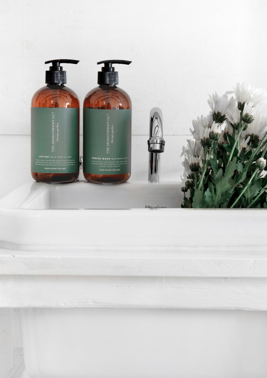 Two Therapy Garden pump bottles beside a chrome tap at a white laundry tub with white daisies