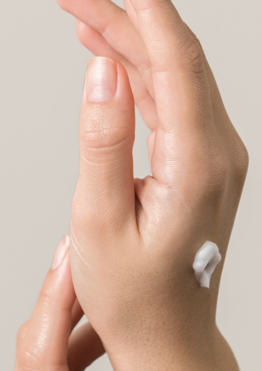 Hand with a dab of white lotion on the back against a warm grey background