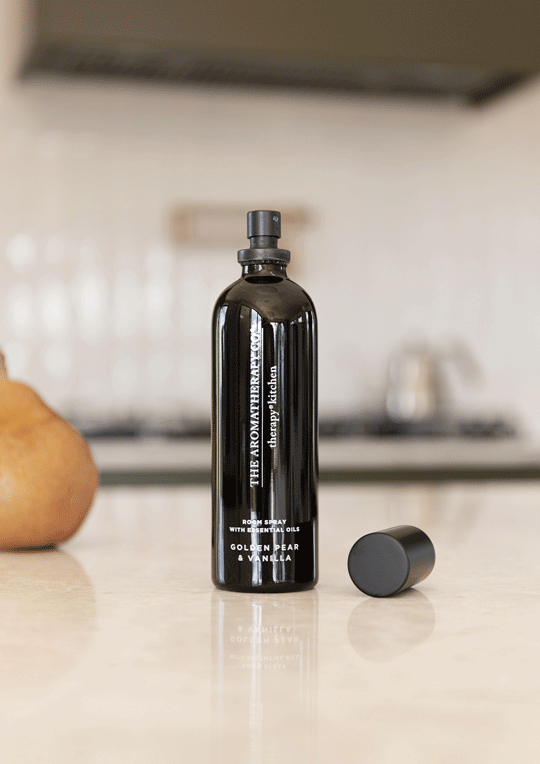 Close view of the Golden Pear & Vanilla spray and its cap on a stone bench with a pear blurred behind