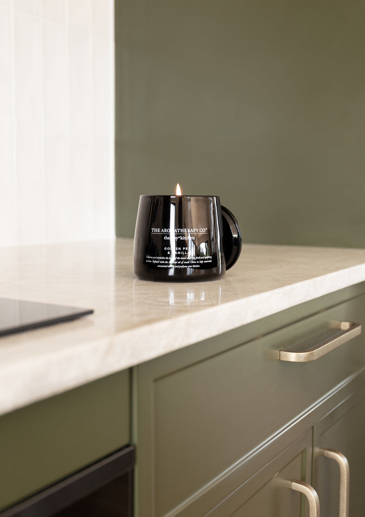 Black Therapy Kitchen candle on a pale benchtop above olive green cabinetry