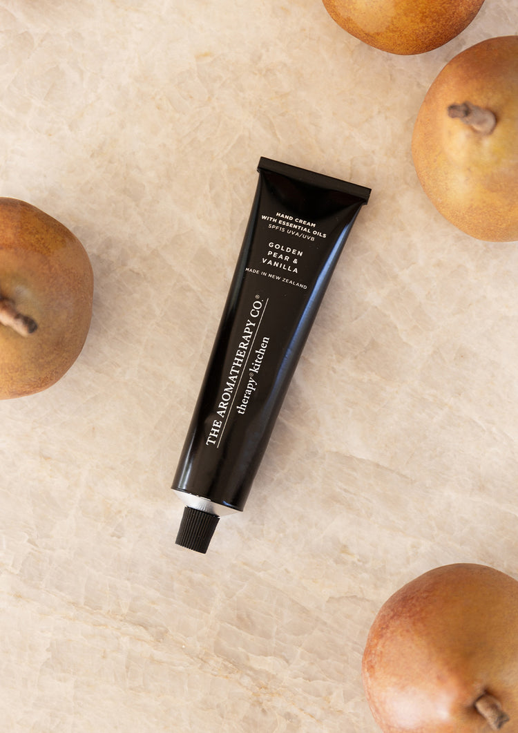 Therapy Kitchen Golden Pear & Vanilla hand cream tube on pale linen surrounded by whole pears