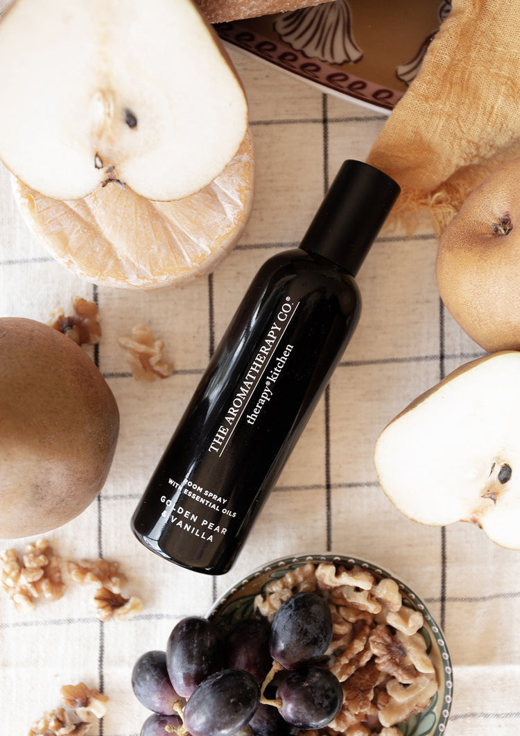 Black room spray lying on a check cloth among halved pears, walnuts and grapes, from above