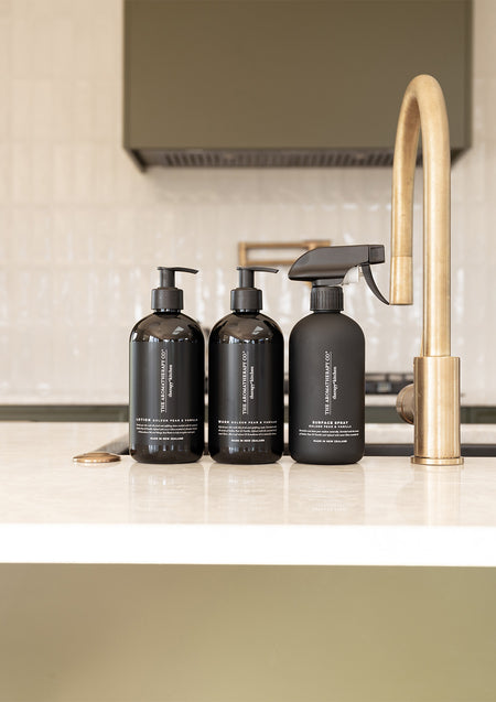 Three black Therapy Kitchen bottles, two pumps and a trigger spray, lined up beside a brass tap