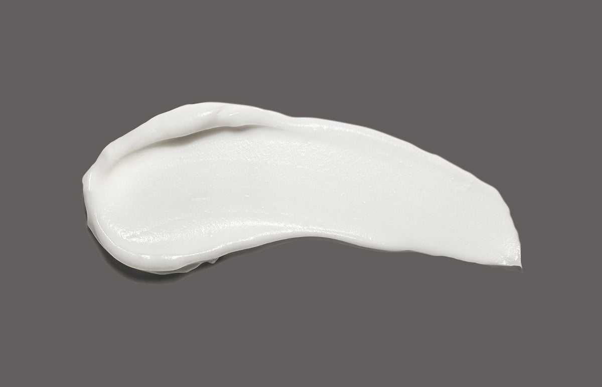 Swatch of white hand cream smeared across a charcoal grey background