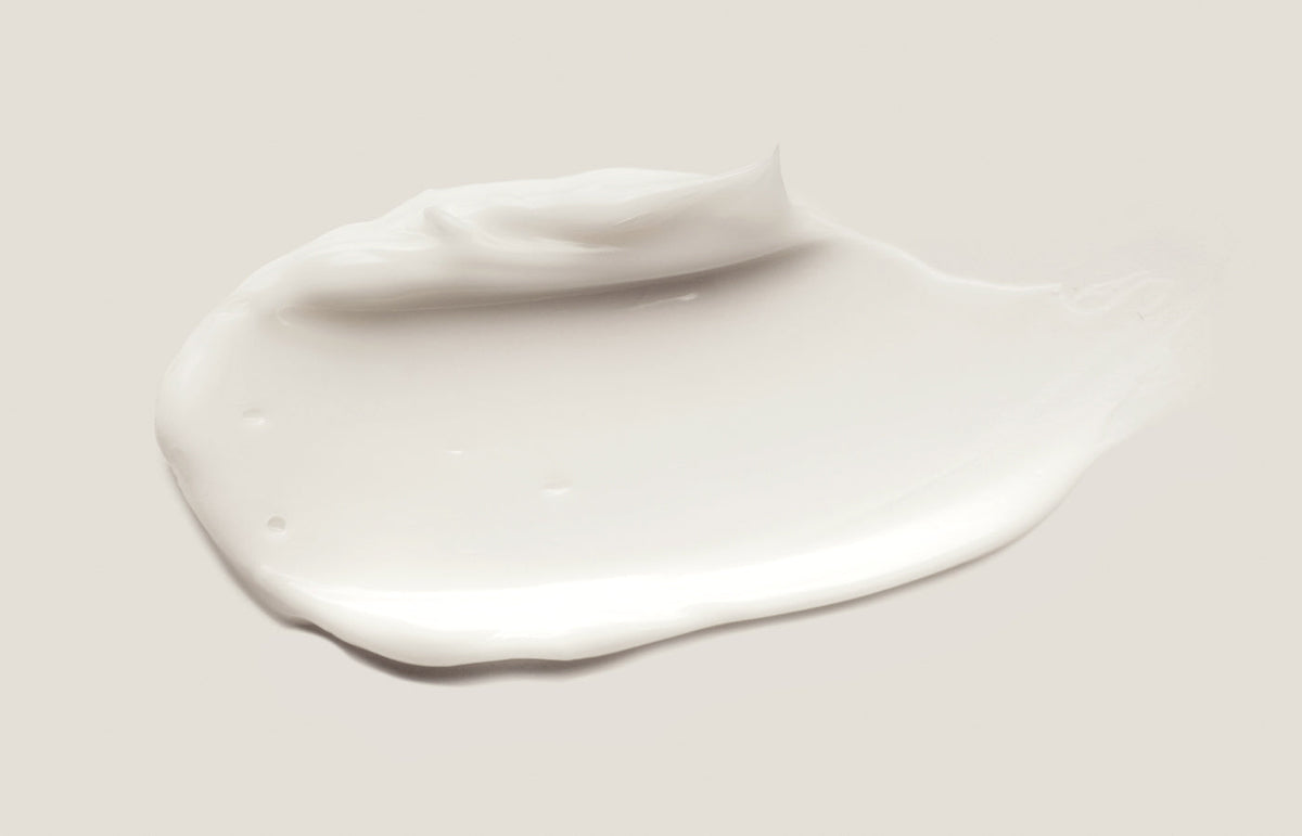 Swatch of white lotion on a pale warm grey background