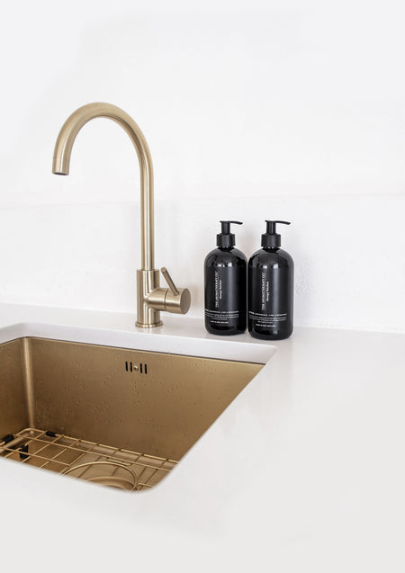 Brass kitchen sink and gooseneck tap with two black Therapy Kitchen bottles on a white bench