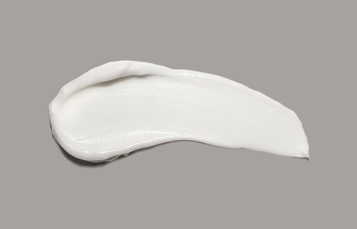 Swatch of white lotion smeared across a warm grey background