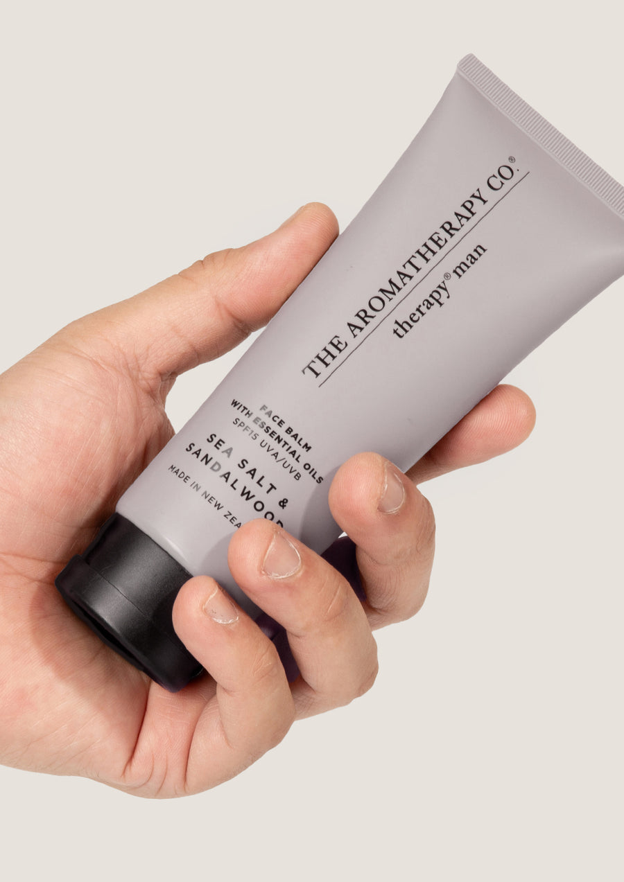 Hand holding the grey Therapy Man face balm tube against a pale grey background