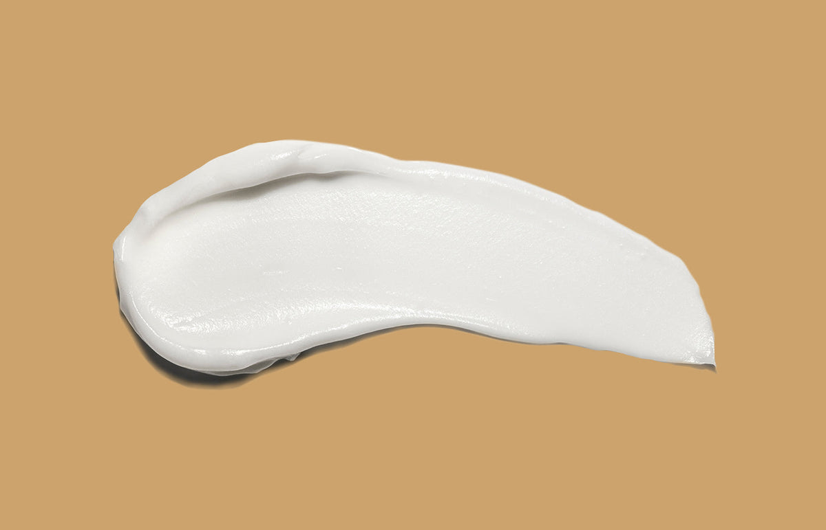 Swatch of white hand cream smeared across a caramel background