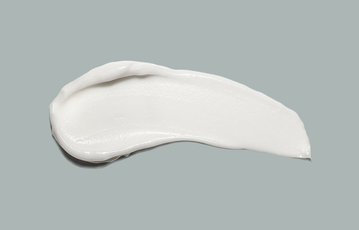 Swatch of white hand cream smeared across a sage grey background