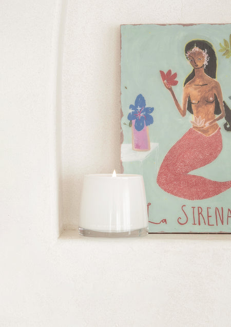 Small white candle in a plaster wall niche beside a colourful mermaid painting
