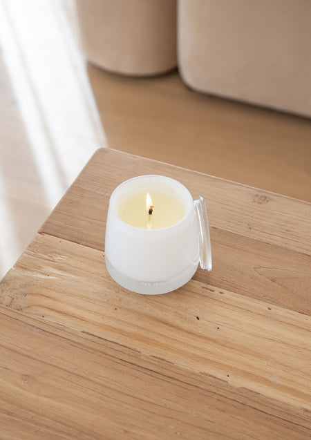 Lit white glass candle with its glass lid on a weathered timber side table